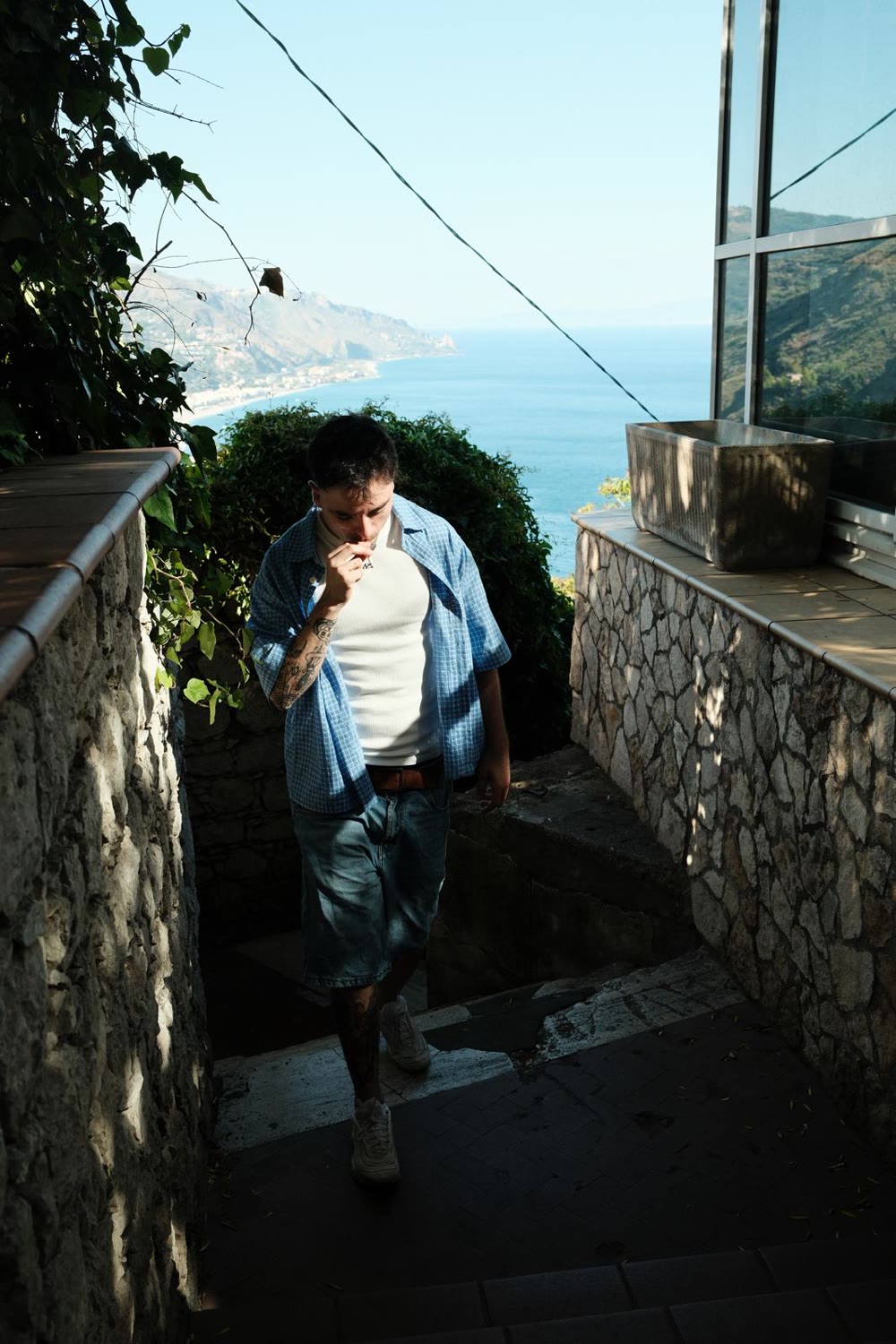 Enzo Ramos walking up stone steps above the sea, smoking