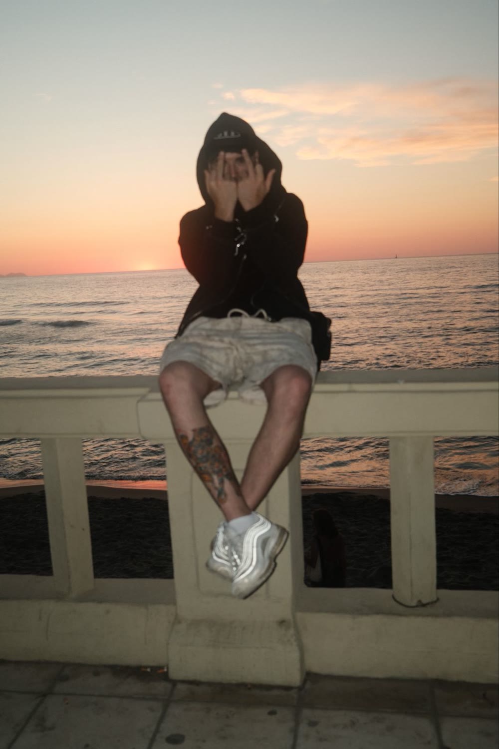 Enzo Ramos sentado en la barandilla del paseo al atardecer, tapándose la cara con las manos